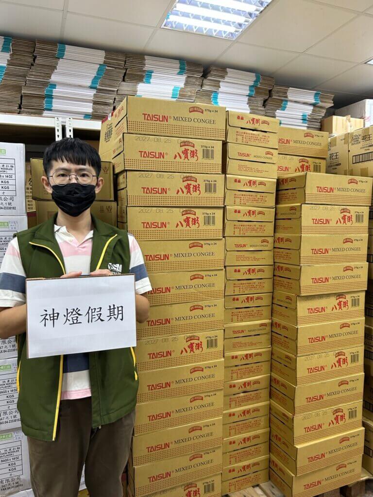 芥菜種會人員手持神燈假期字牌，身後為整疊泰山八寶粥紙箱